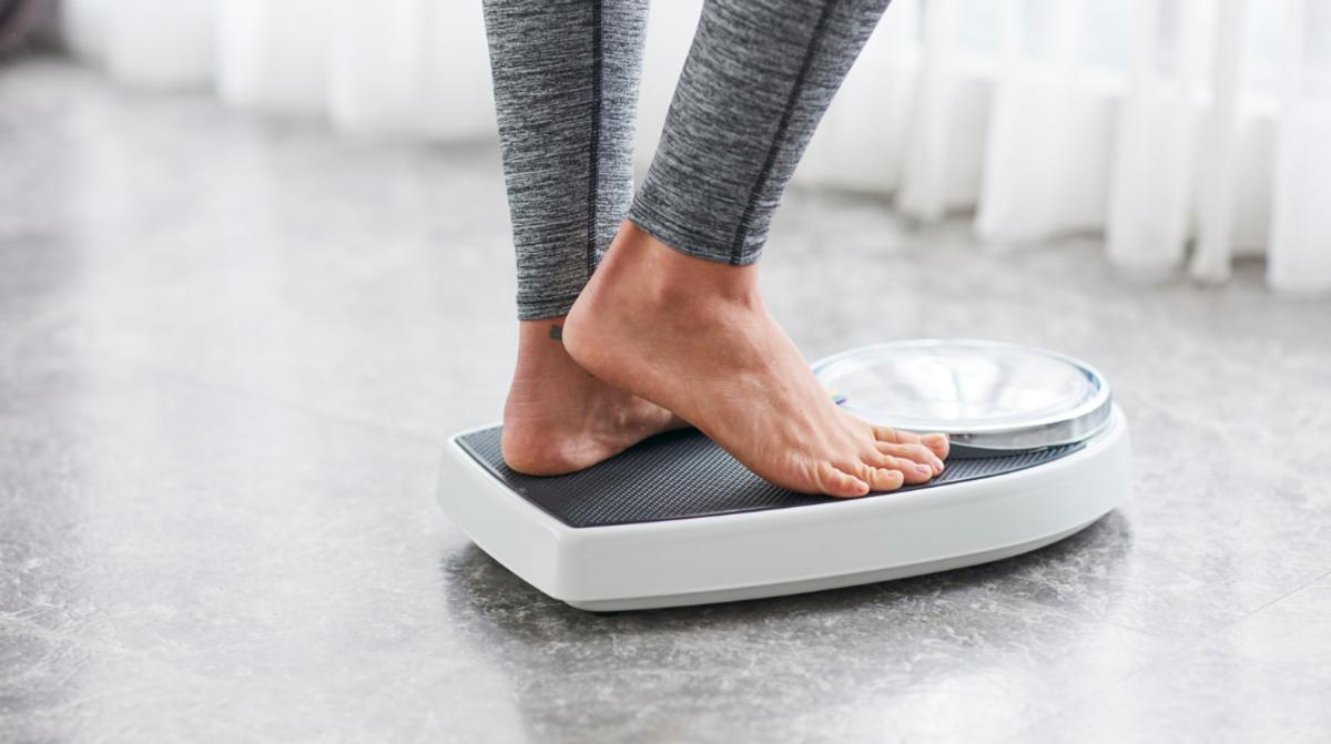 A woman wearing gray leggings standing on a bathroom scale